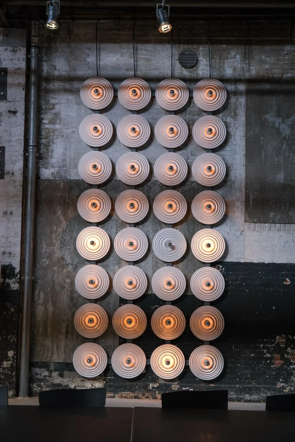 Frontaal overzicht van The Ripple met ronde lichtobjecten op een ruwe wand